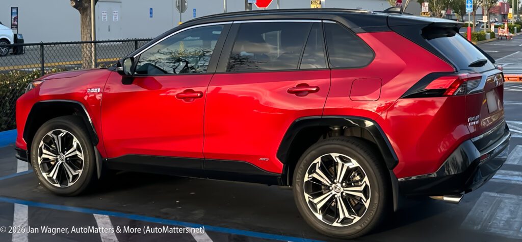 A red and black Toyota RAV4 Prime SUV is parked in a parking lot near a blue-striped accessible parking space.