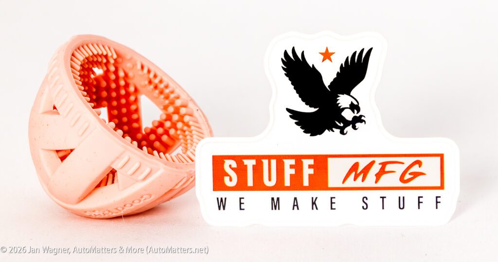A textured, peach-colored rubber ball sits next to a "STUFF MFG WE MAKE STUFF" sticker with a black eagle and orange star on a white background.