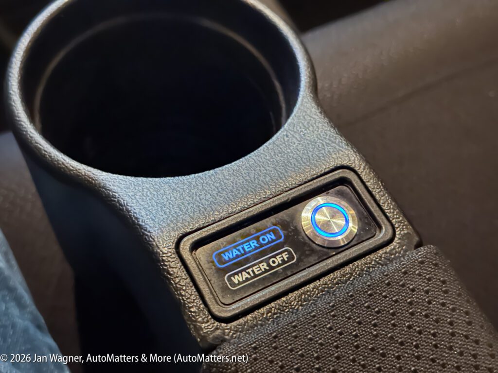 Close-up of a car console showing a cup holder and a control panel with buttons labeled "WATER ON" and "WATER OFF" beside a blue-lit circular dial.