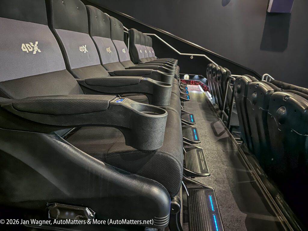 Rows of black 4DX cinema seats with cup holders, motion platforms, and illuminated blue footrests inside a modern movie theater.