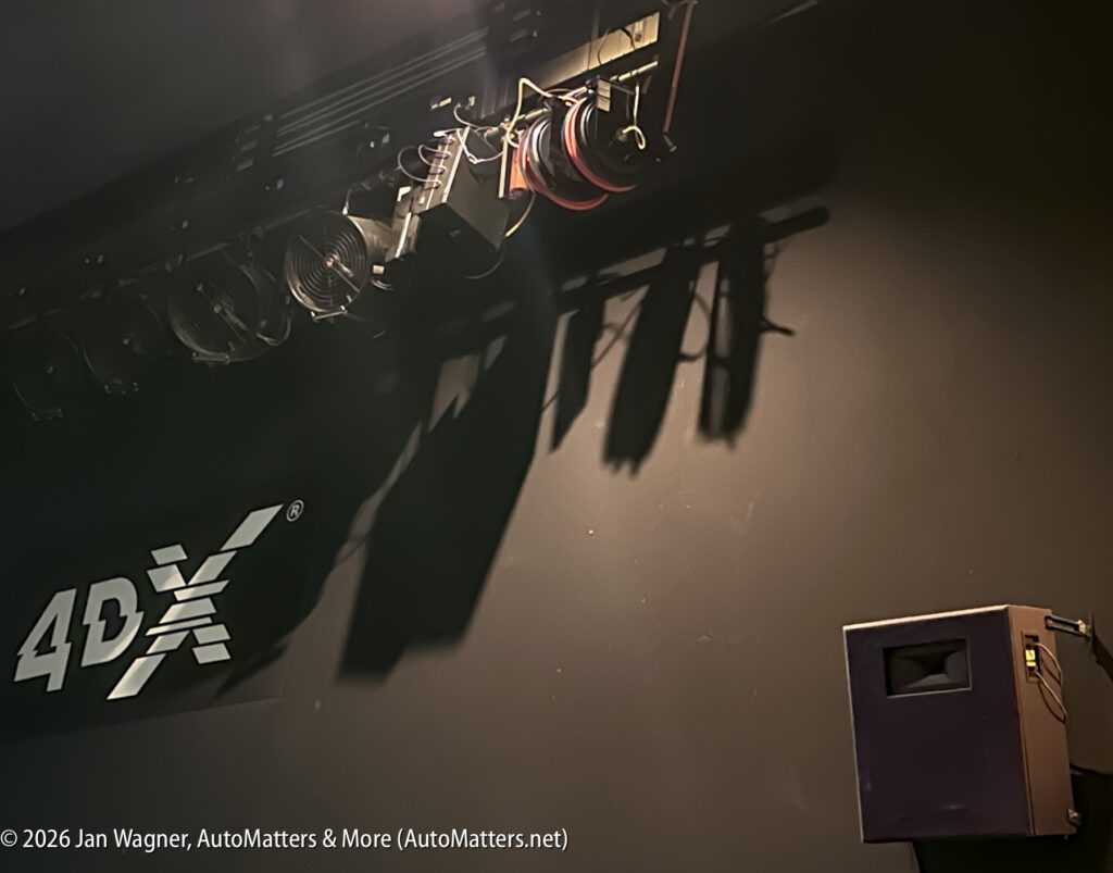 Stage lighting equipment and cables mounted on a ceiling above a 4DX logo, with a speaker attached to the wall on the right.