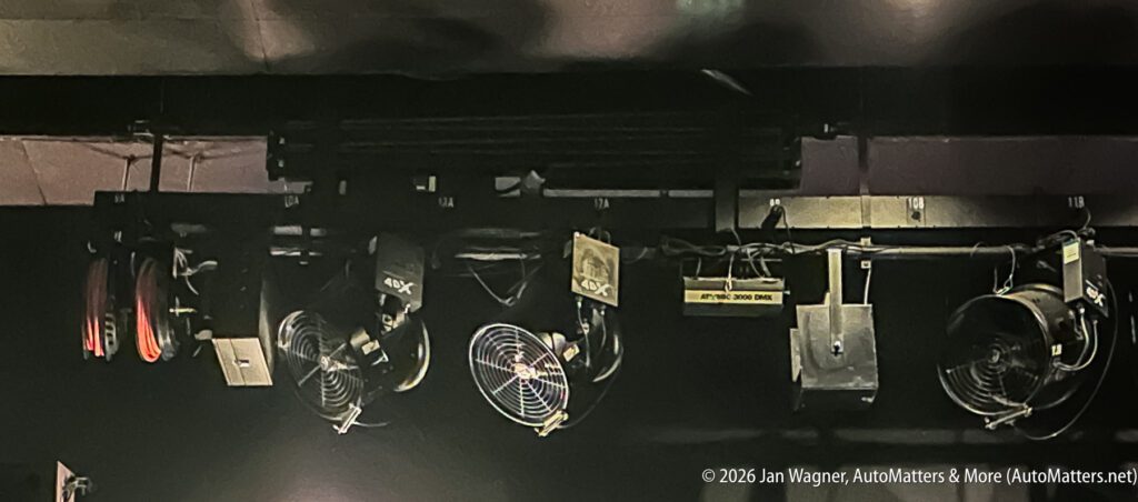 Ceiling-mounted stage equipment including fans, lights, cables, and power outlets in a dimly lit area.