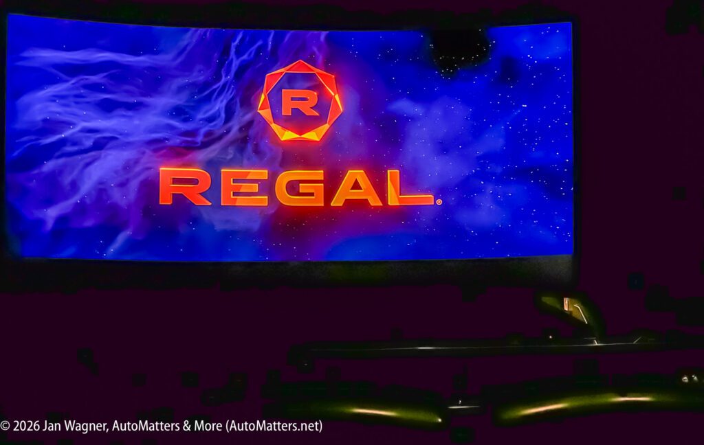 A movie theater screen displays the Regal logo in orange with a blue cosmic background. Theater seats are visible in the foreground.