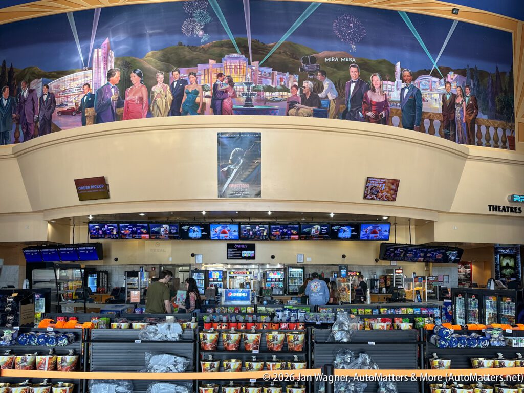 Movie theater concession stand with snacks, drinks, and merchandise; above is a mural depicting people and Las Vegas landmarks with fireworks in the background.