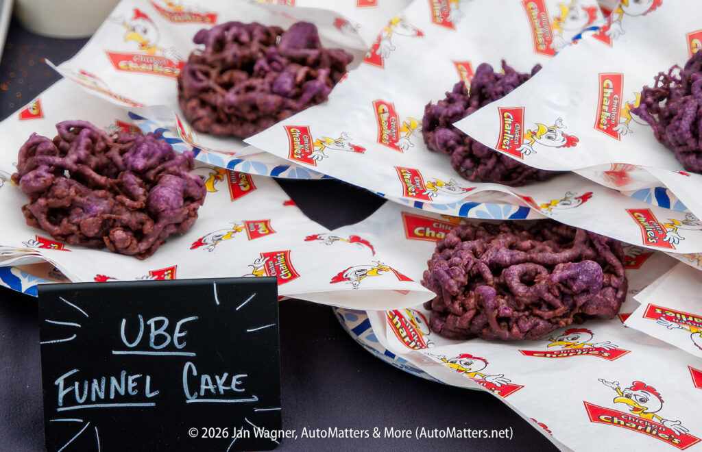 Plates of purple ube funnel cake are displayed on branded paper with a small chalkboard sign reading "UBE Funnel Cake.