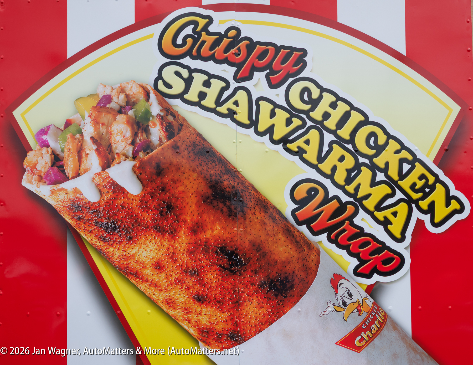 A sign advertises a crispy chicken shawarma wrap with an image of the wrap filled with chicken, onions, and vegetables on a red and yellow background.