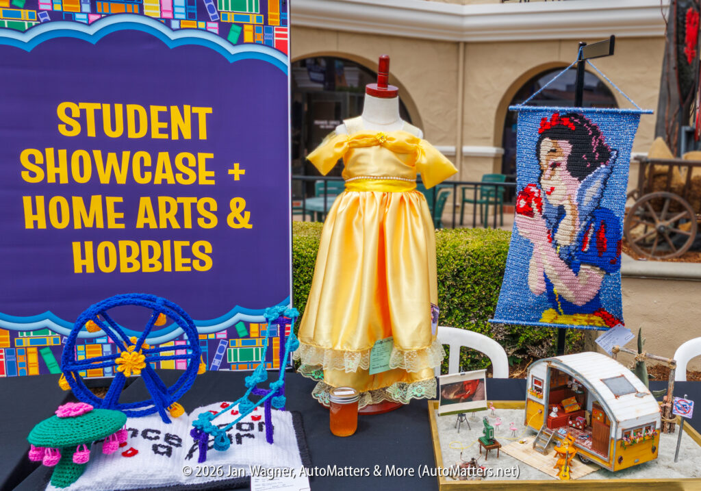 Table with a yellow dress, Snow White tapestry, small Ferris wheel model, camper diorama, and sign reading "Student Showcase + Home Arts & Hobbies.