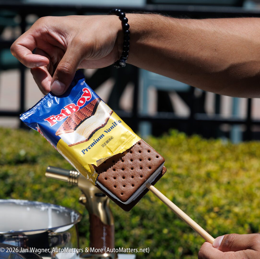 A hand holds a FatBoy Premium Vanilla ice cream sandwich, partially unwrapped and speared with a wooden stick over a metal pot.