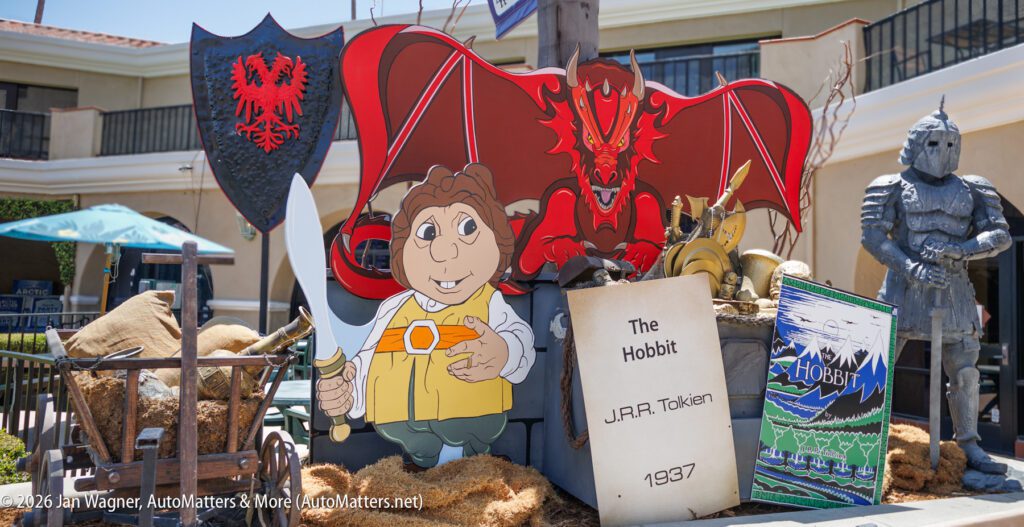 Display featuring a large cartoon hobbit, a red dragon, armor, shields, and props with "The Hobbit" and "J.R.R. Tolkien 1937" on an open book, set outdoors.