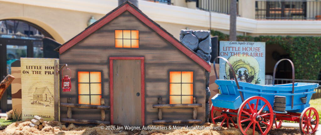 A display features a small wooden house, a blue wagon, a lantern, and books titled "Little House on the Prairie" by Laura Ingalls Wilder.
