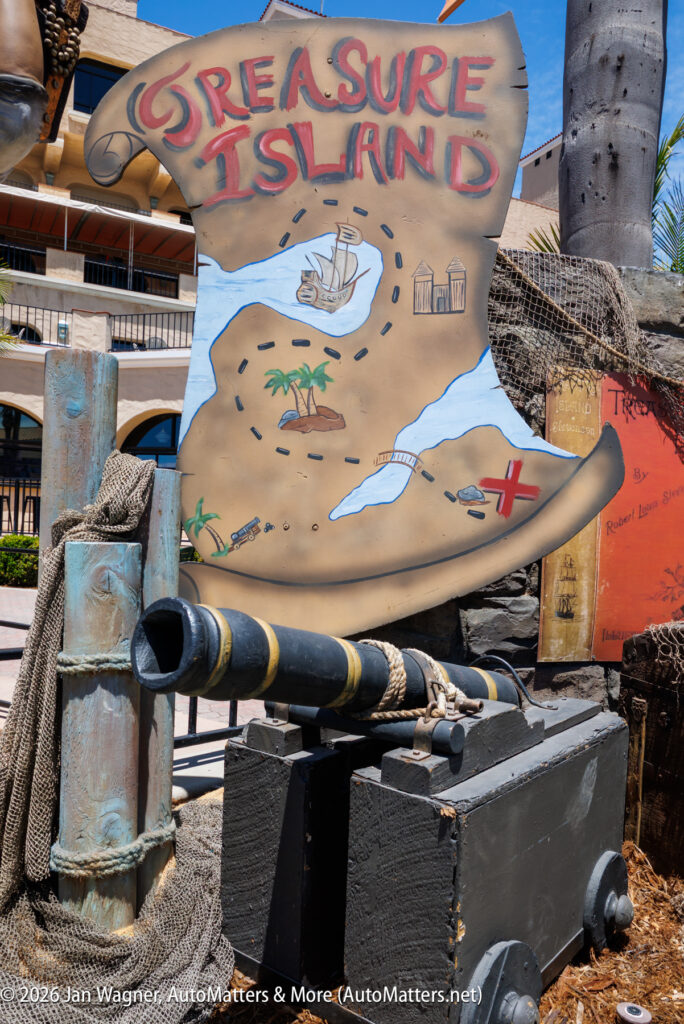A painted "Treasure Island" map sign with a cannon in front, surrounded by nautical props and netting, displayed outdoors near a building.