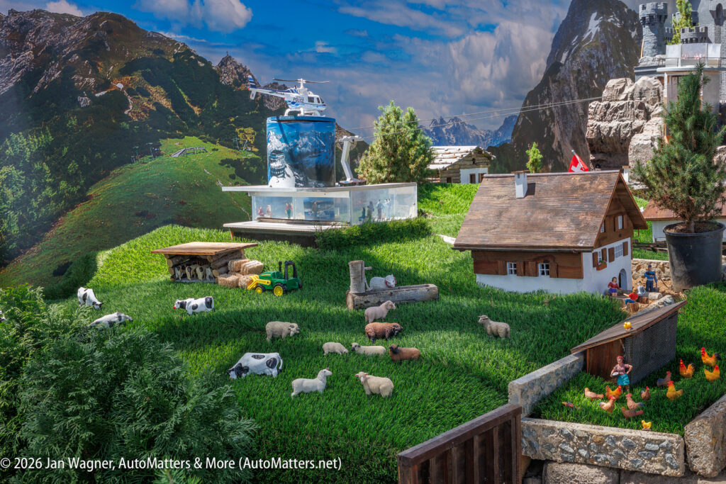 A detailed miniature model displays a farm scene with cows, sheep, goats, chickens, tractors, farmhouses, and mountains in the background.