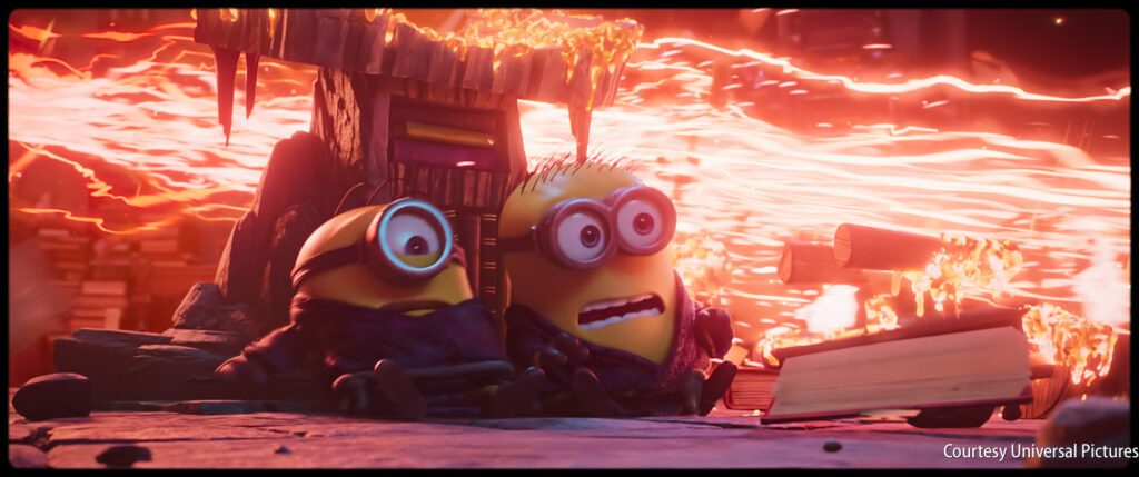 Two Minions sit in front of a hut as streams of lava flow behind them, with shocked expressions on their faces.