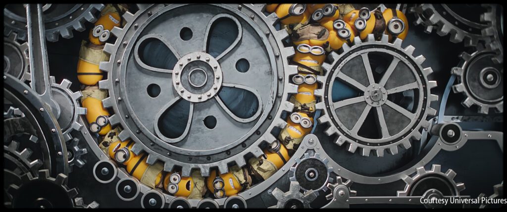 Minions are crowded between large interlocking gears and cogs, wearing goggles and blue overalls, inside an industrial machine.