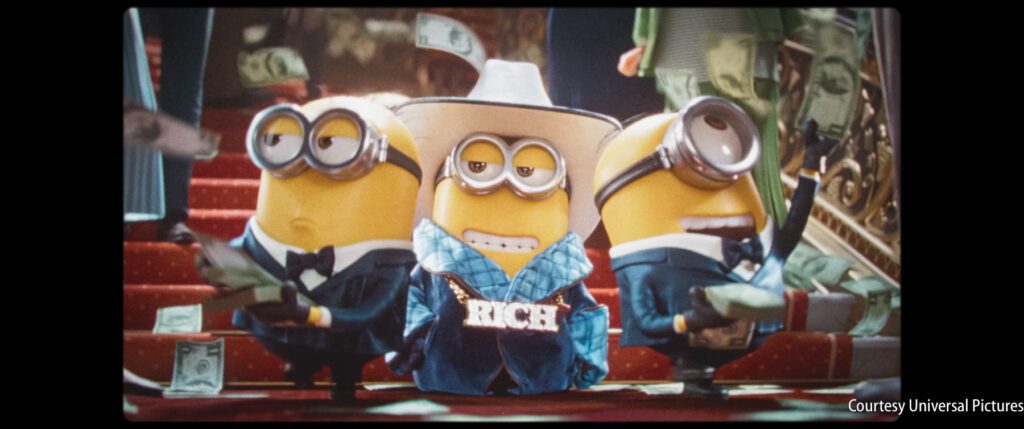 Three Minions in tuxedos and a cowboy hat stand on red stairs, with dollar bills falling around them. The center Minion wears a necklace that says "RICH.