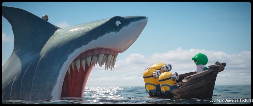 A giant shark with its mouth open faces three yellow Minions and a green character in a small wooden boat on the ocean.