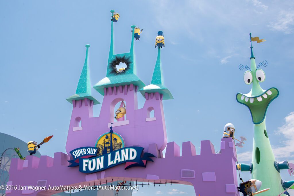 A colorful castle at Super Silly Fun Land features Minions on the towers and a whimsical green character beside it under a partly cloudy sky.