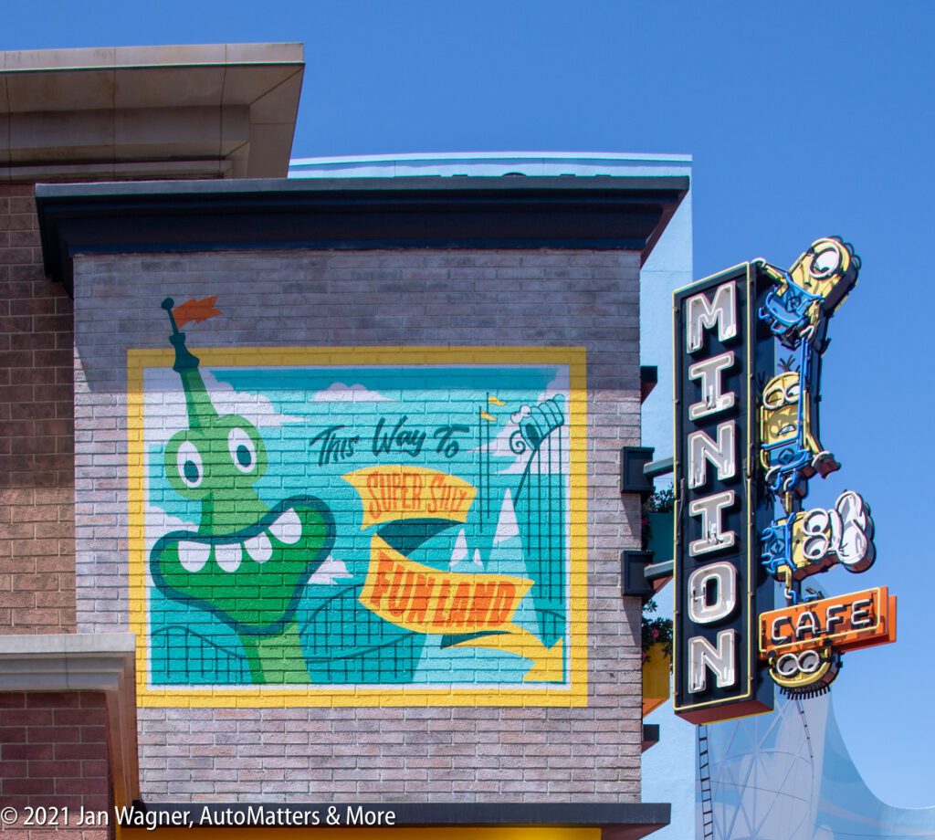 A colorful mural and a Minion Cafe sign are displayed on a brick building under a clear blue sky.