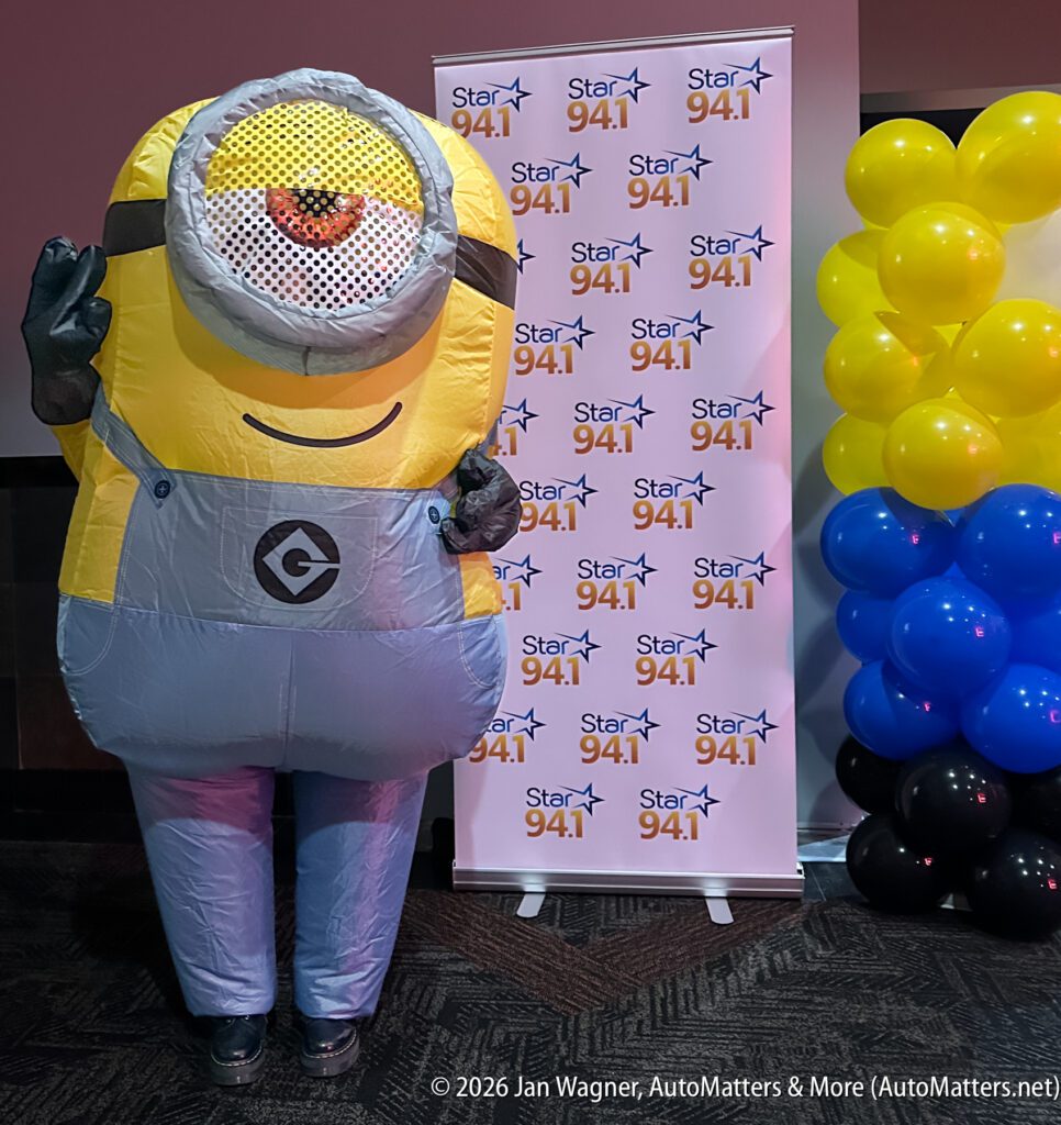 A person in a Minion costume stands in front of a Star 94.1 banner next to a column of yellow and blue balloons.
