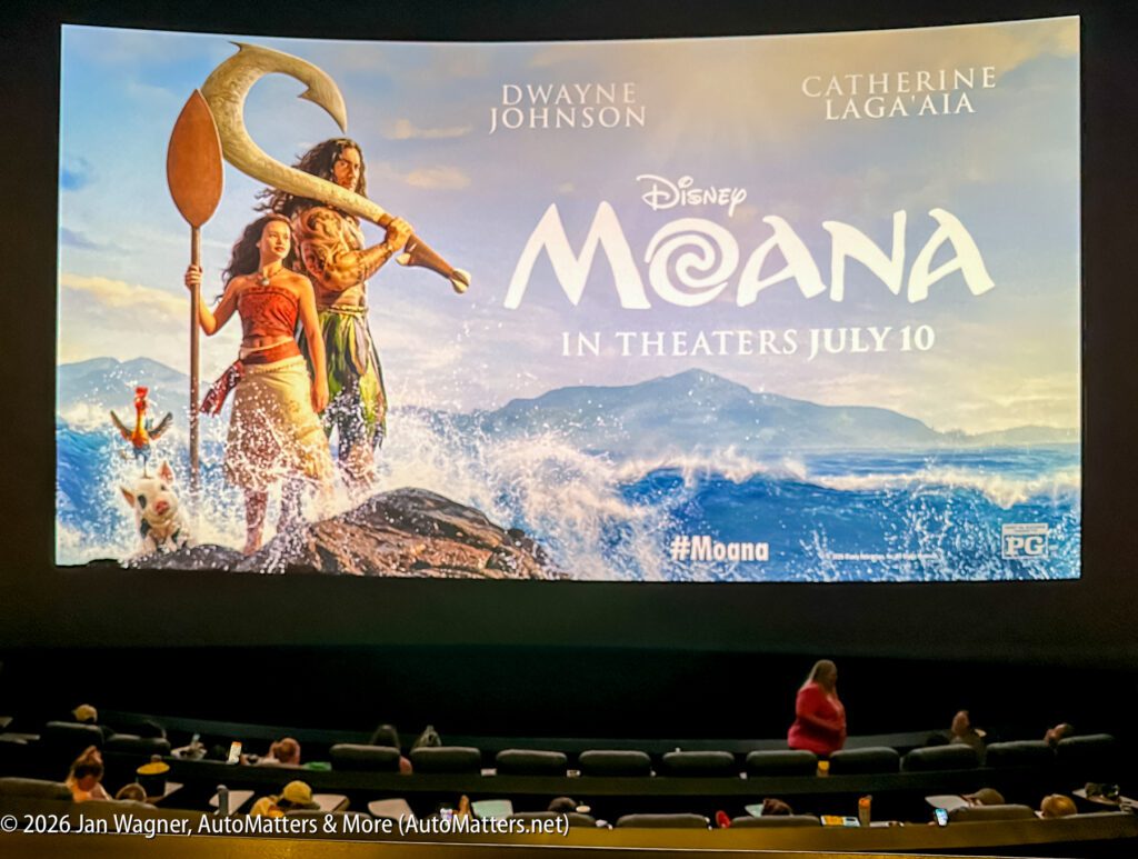 A movie theater screen displays a "Moana" movie poster featuring Moana and Maui, with audience members seated below.