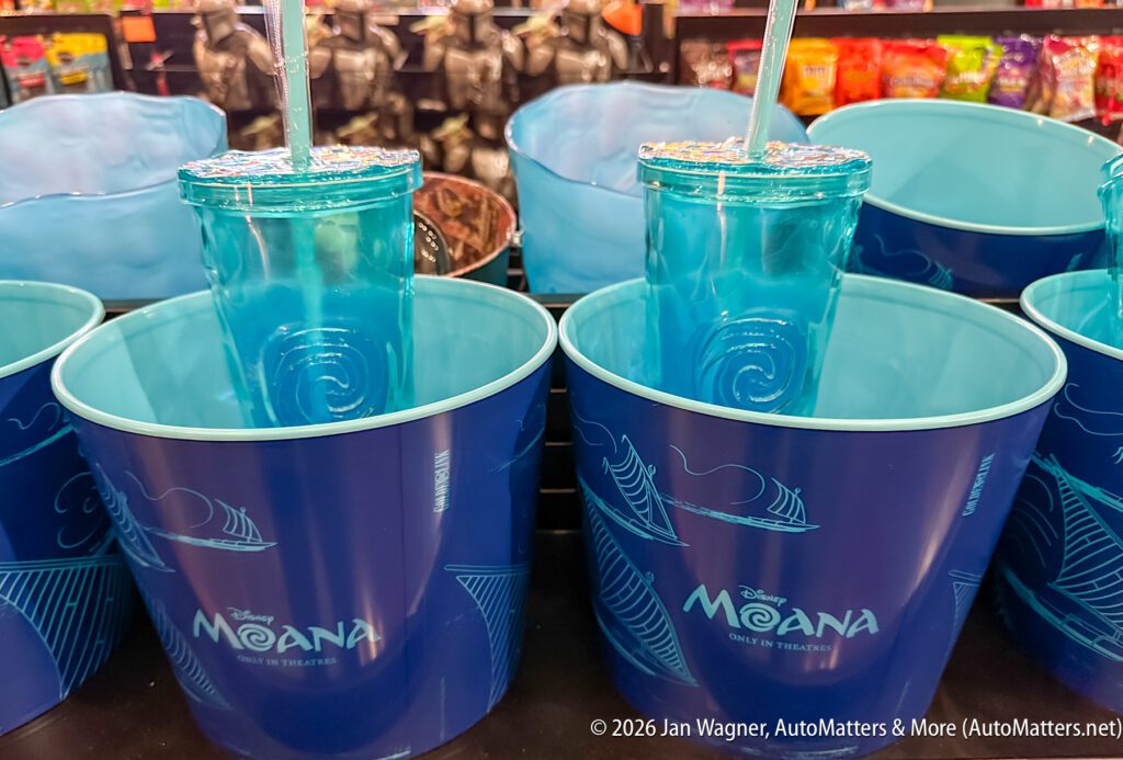 Blue Disney Moana-themed cups with straws are placed inside matching blue Moana popcorn buckets on a store display shelf.