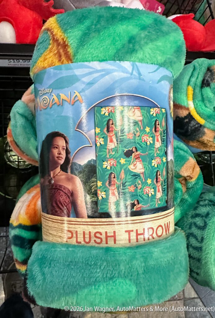 A Moana-themed plush throw blanket with an image of Moana on the label and a sample pattern featuring Moana and tropical designs.