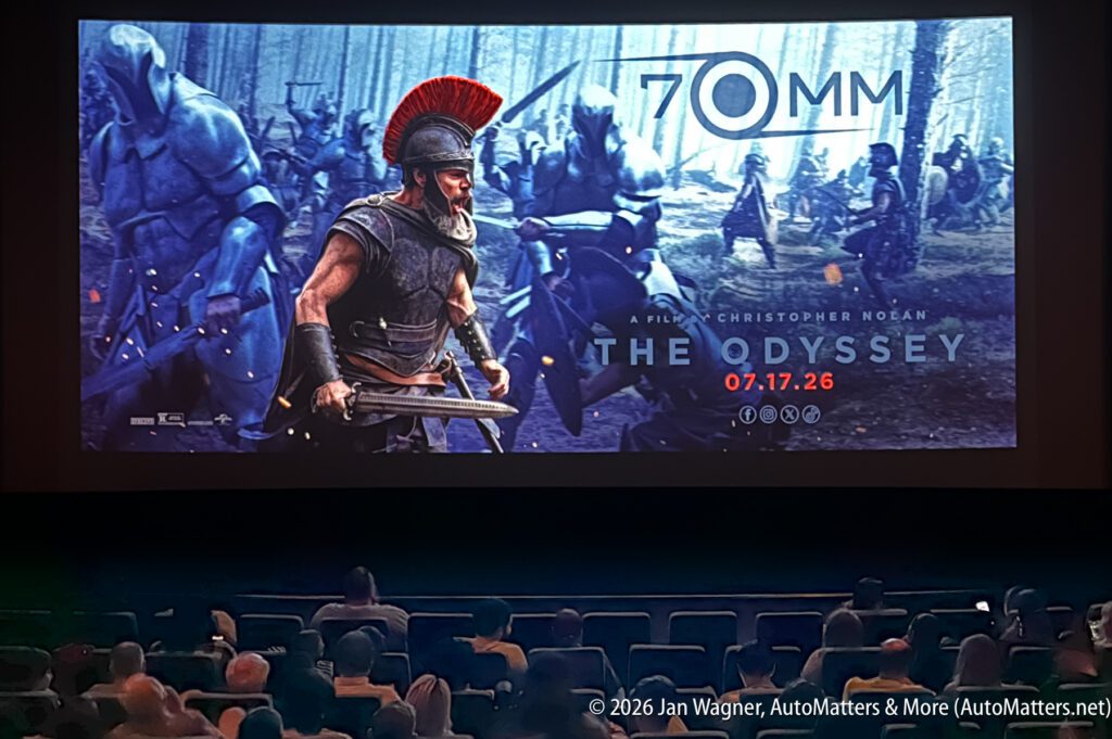 A movie audience watches a large screen displaying a 70mm film poster for "The Odyssey," directed by Christopher Nolan, with a release date of July 17, 2026, featuring ancient warriors.