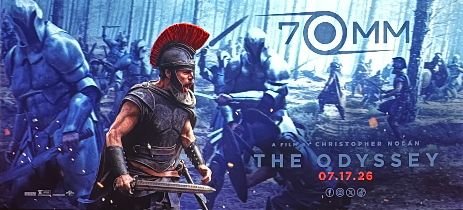 A Roman soldier with a red plume leads troops in battle; text reads "70MM," "THE ODYSSEY," "A FILM BY CHRISTOPHER NOLAN," and "07.17.26" with rating icons below.