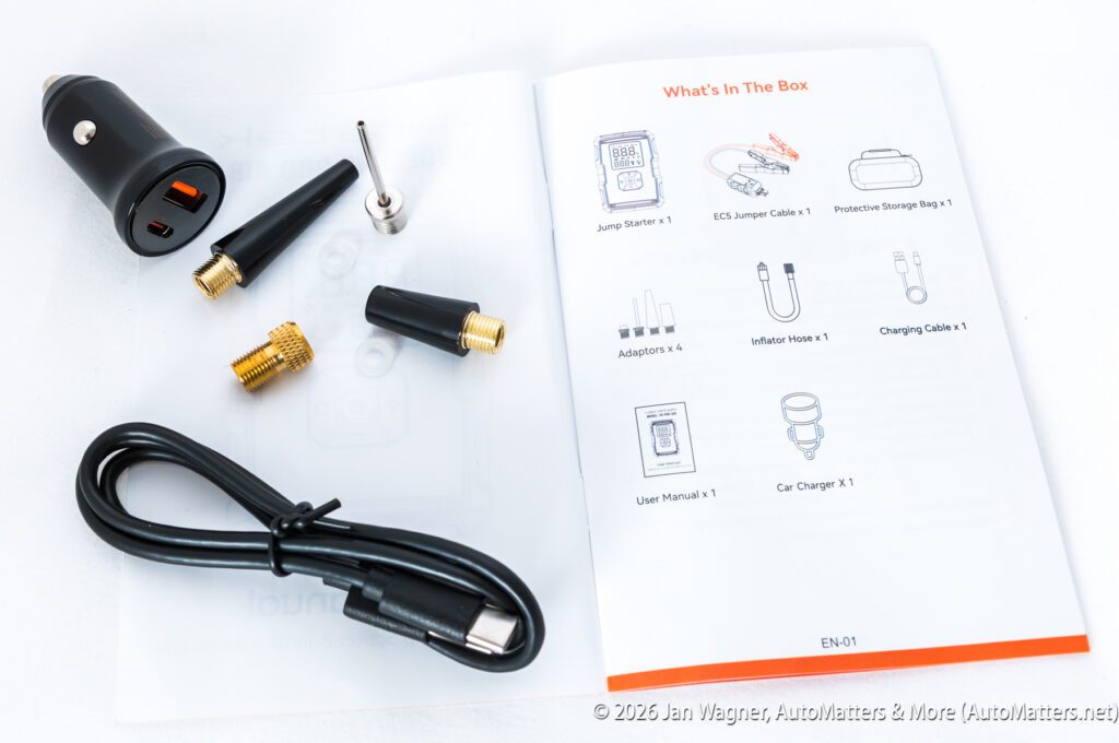 A jump starter kit with adapters, cables, and an open manual displaying “What’s In The Box” with item illustrations and labels.