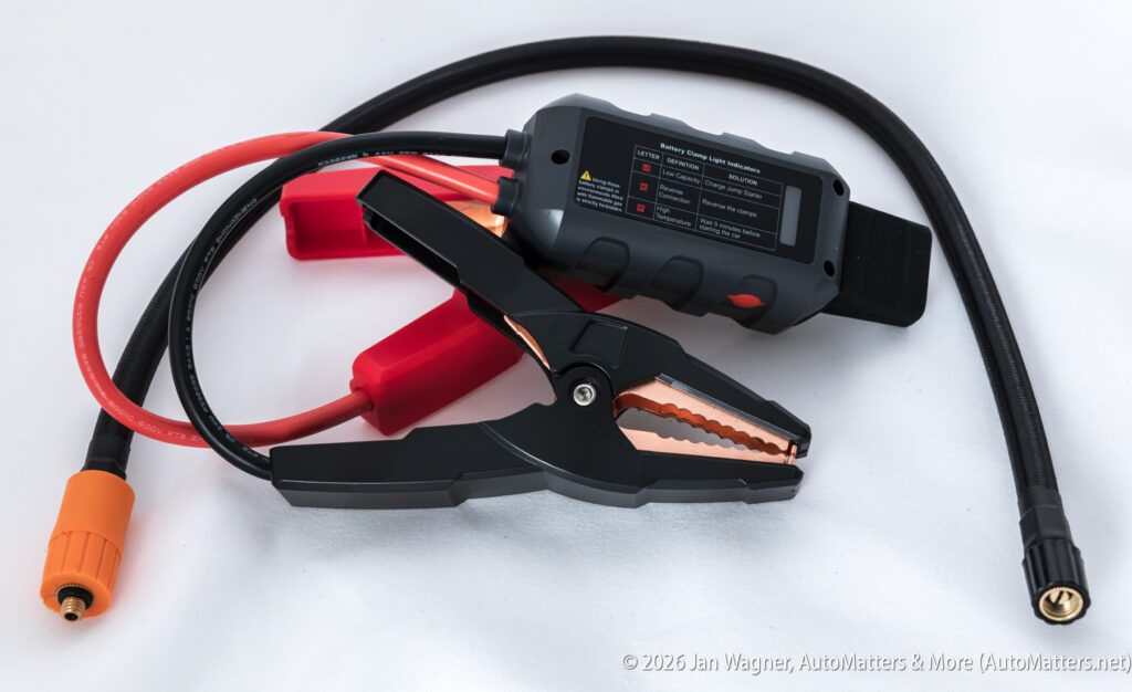 A portable car jump starter with attached jumper cables, an orange connector, and a black hose, displayed on a white surface.