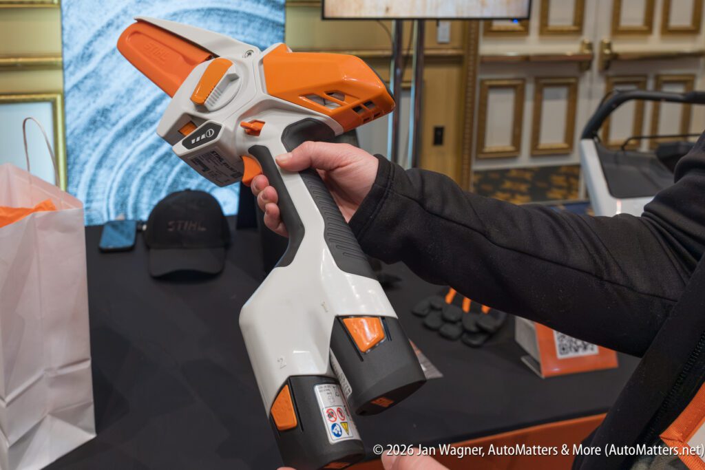 A person holds an orange and white STIHL battery-powered tool at an indoor event display.