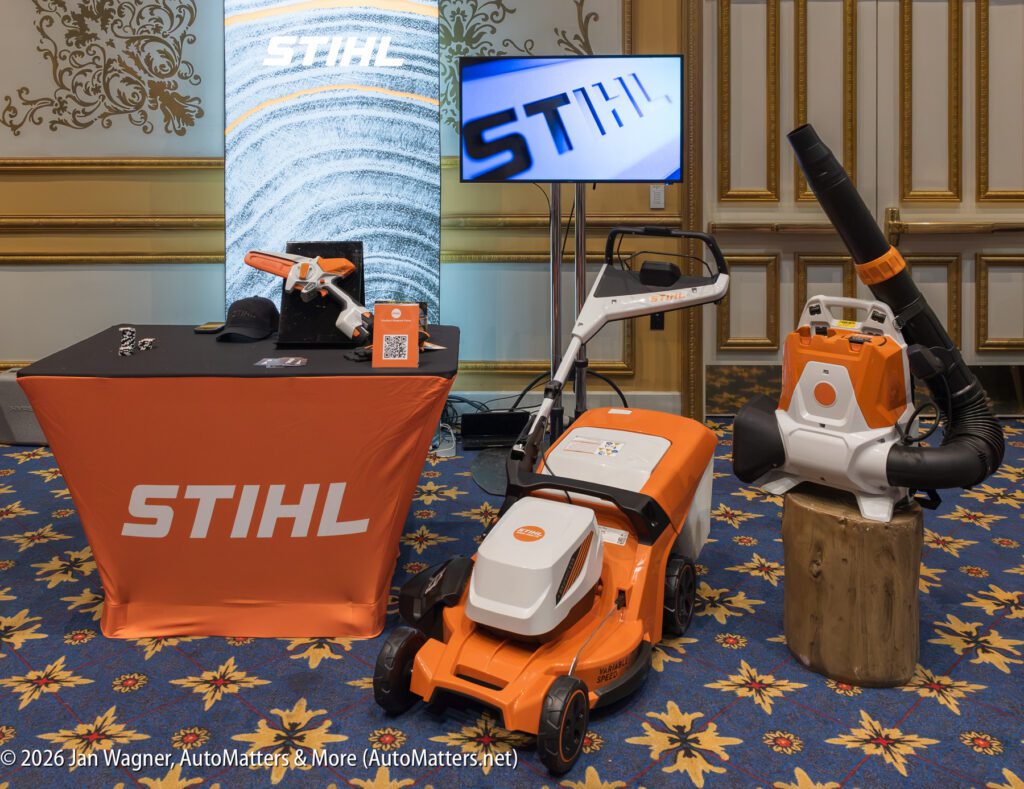 STIHL branded display with battery-powered lawn mower, leaf blower, trimmer, and promotional materials set up in a decorated indoor venue.