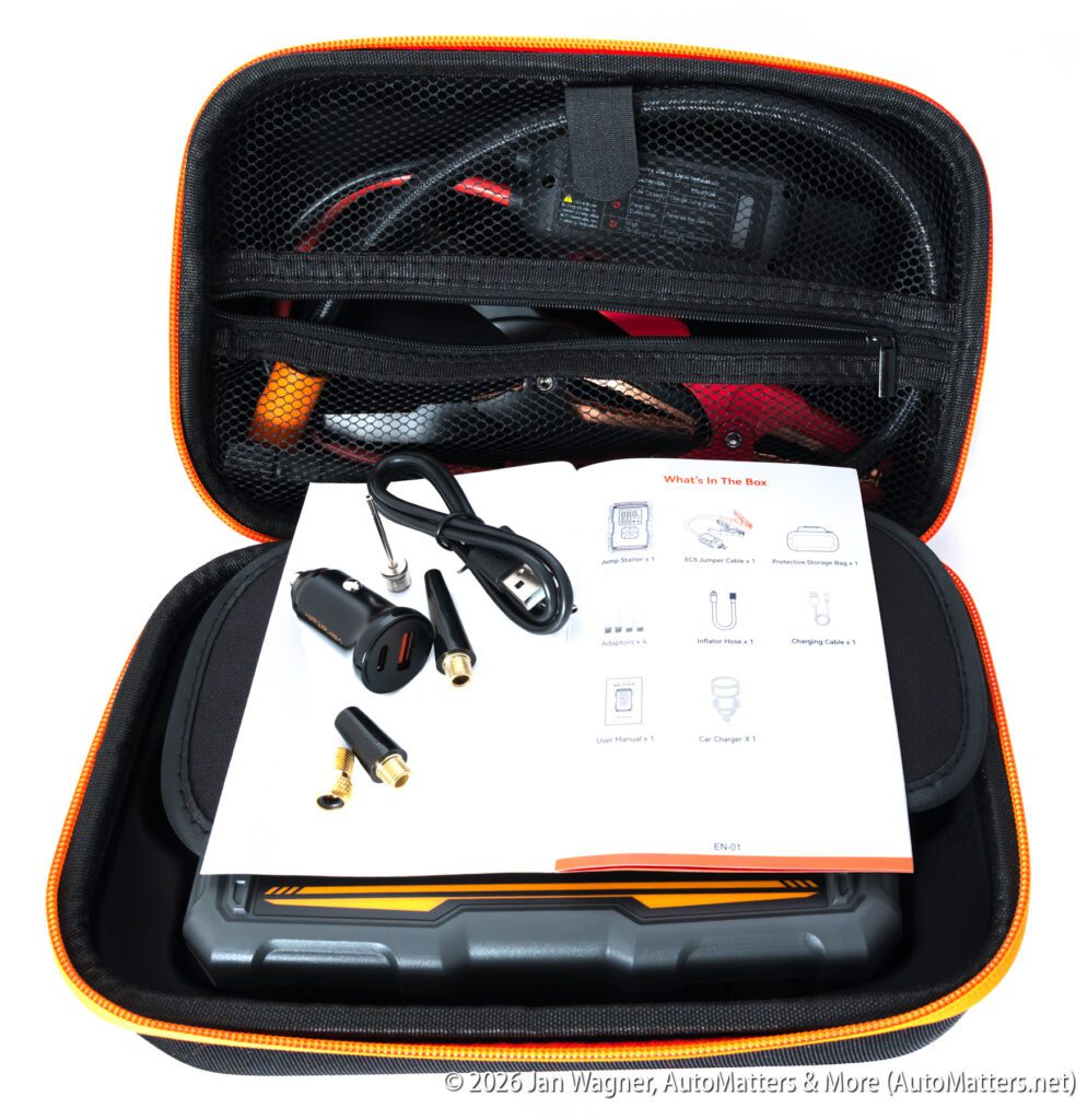 A portable car jump starter kit in an open zippered case, showing cables, user manual, adapters, and a charger.