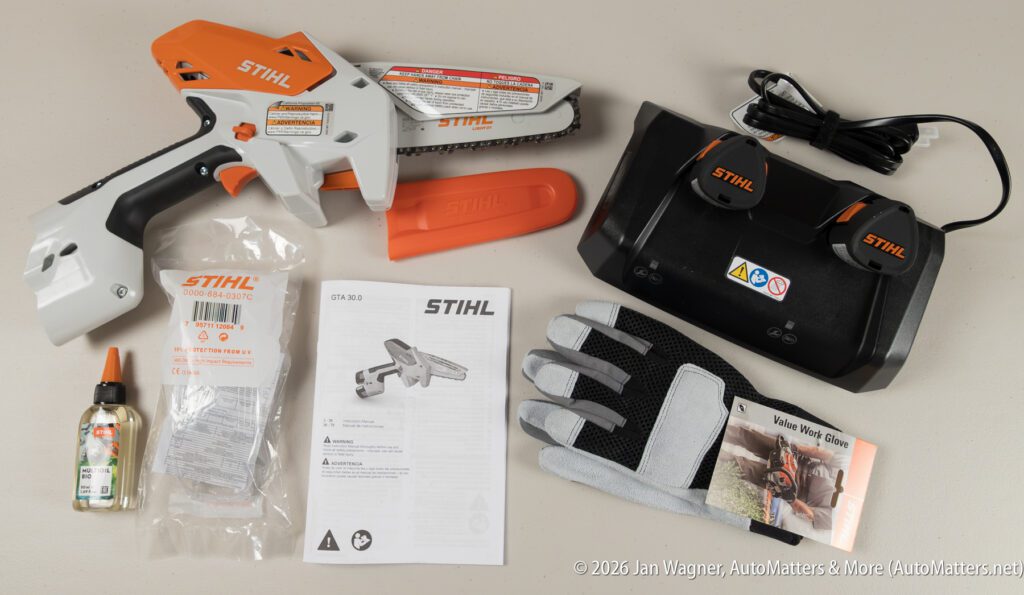 STIHL GTA 26 pruning saw kit with saw, blade cover, two batteries, charger, gloves, oil, manual, and safety instructions arranged on a light surface.