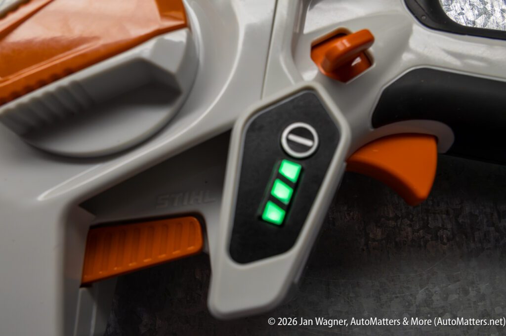 Close-up of a gray and orange power tool handle with two green indicator lights illuminated and a plus-minus symbol above the lights.