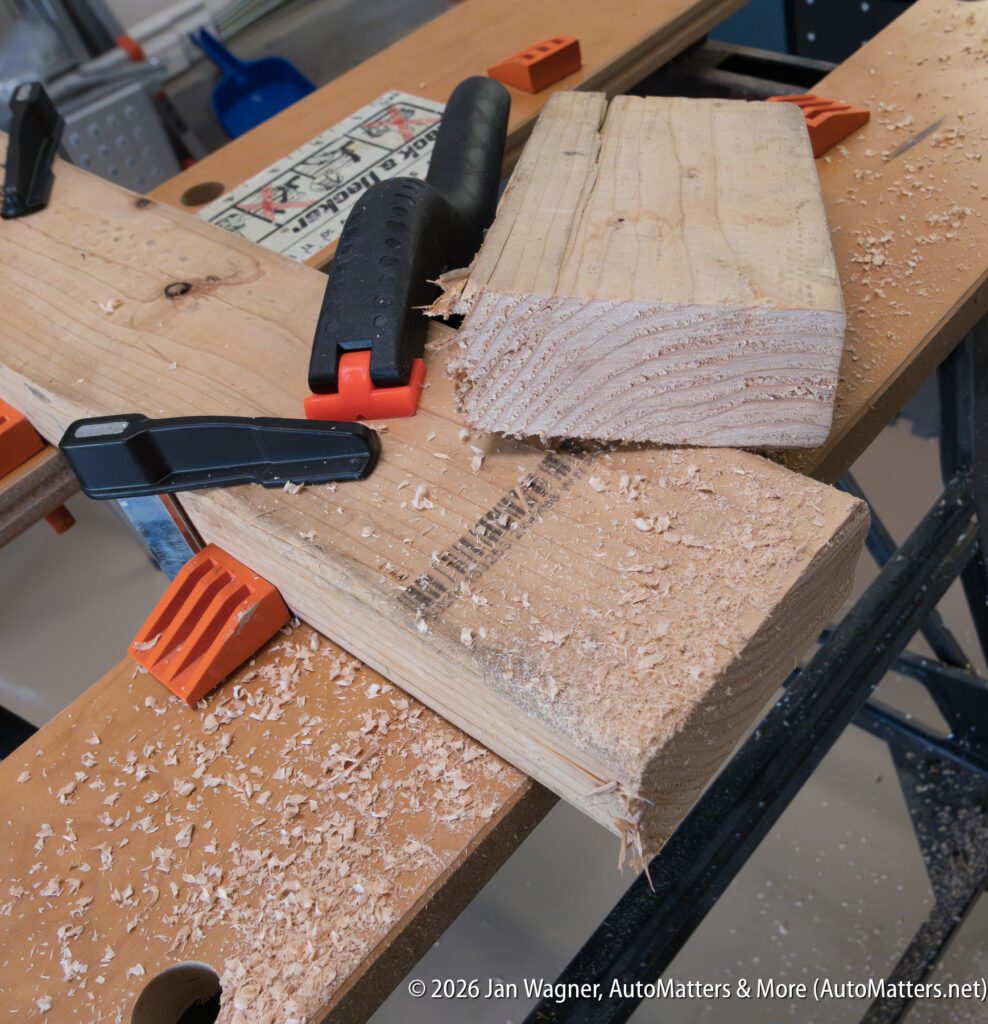A workbench with clamps holding two pieces of wood, one partially sawed; wood shavings are scattered on the surface.