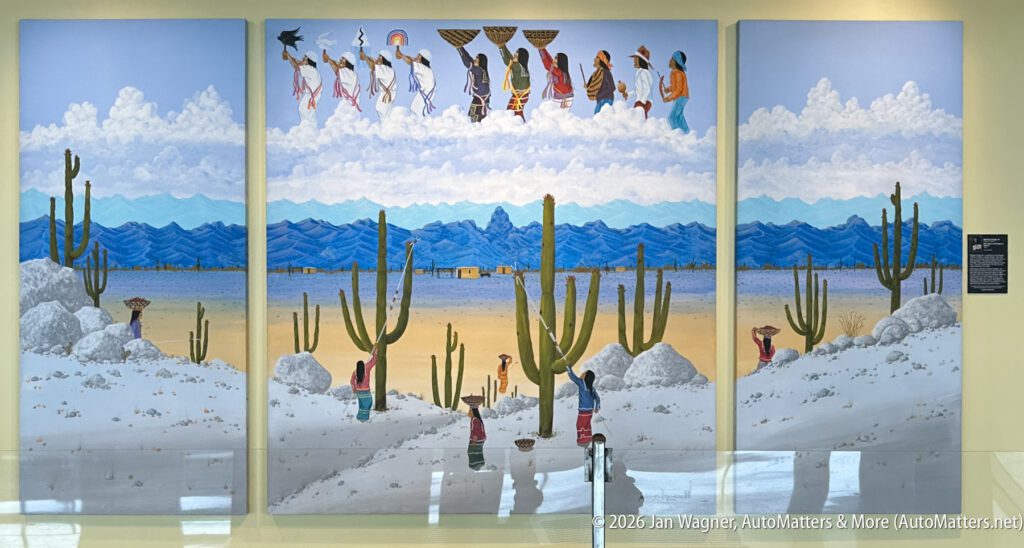 Three-panel mural shows people walking with baskets in a desert landscape with cacti and mountains; some figures appear above the clouds while others walk among cacti on rocky ground.