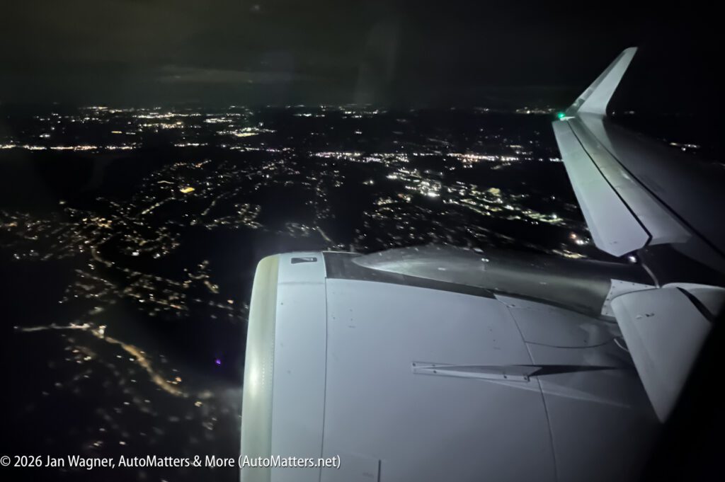 View from an airplane window at night, showing the wing, engine, and city lights below.