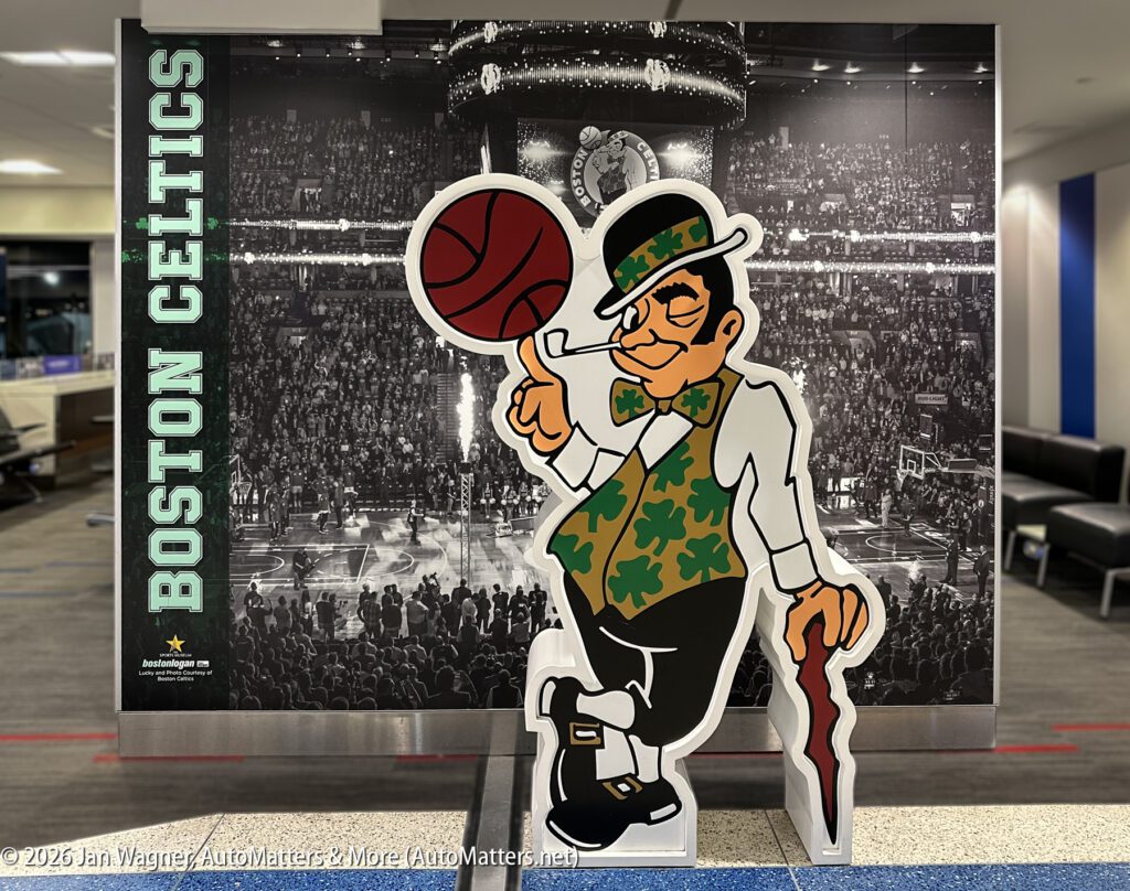 Cutout of the Boston Celtics leprechaun mascot in front of a black-and-white photo of a basketball arena with “Boston Celtics” text on the left.