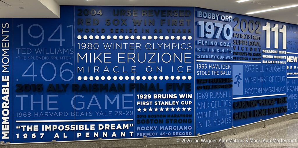 Blue wall mural displays significant Boston sports moments and athletes, including dates, events, and names such as Ted Williams, Mike Eruzione, Aly Raisman, and Bobby Orr.