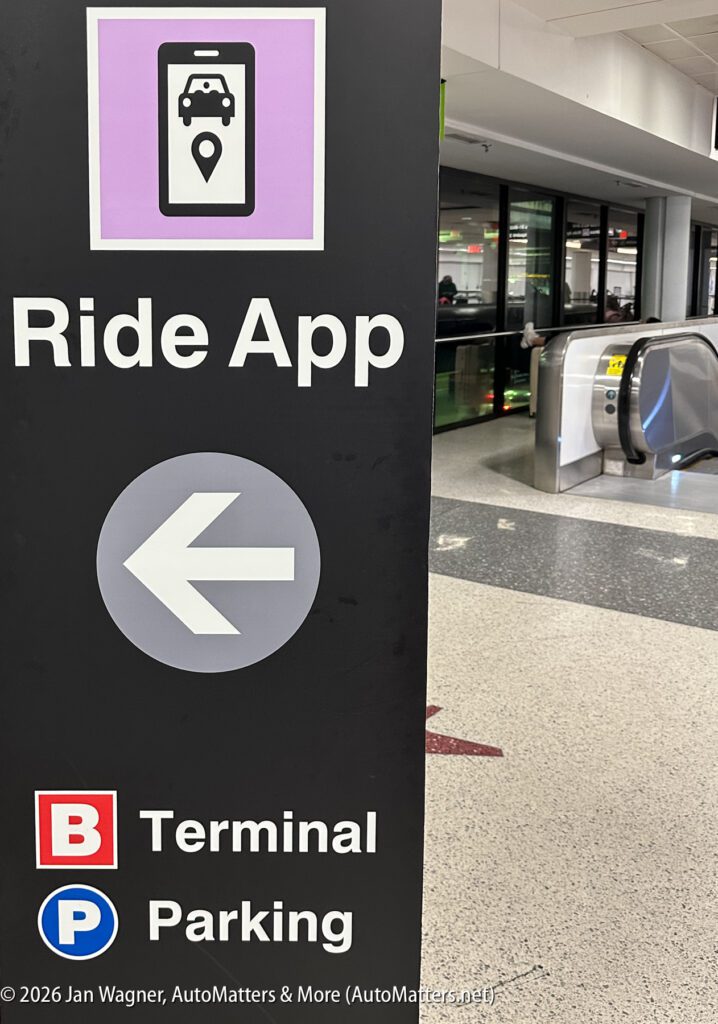 Sign in airport shows “Ride App” with left arrow, directions to B Terminal, and Parking. Escalator and windows are visible in background.