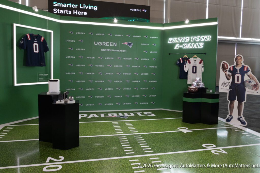 Exhibit booth with UGREEN branding, football jerseys, a cardboard player cutout, and electronics on display, set on a floor resembling a football field.