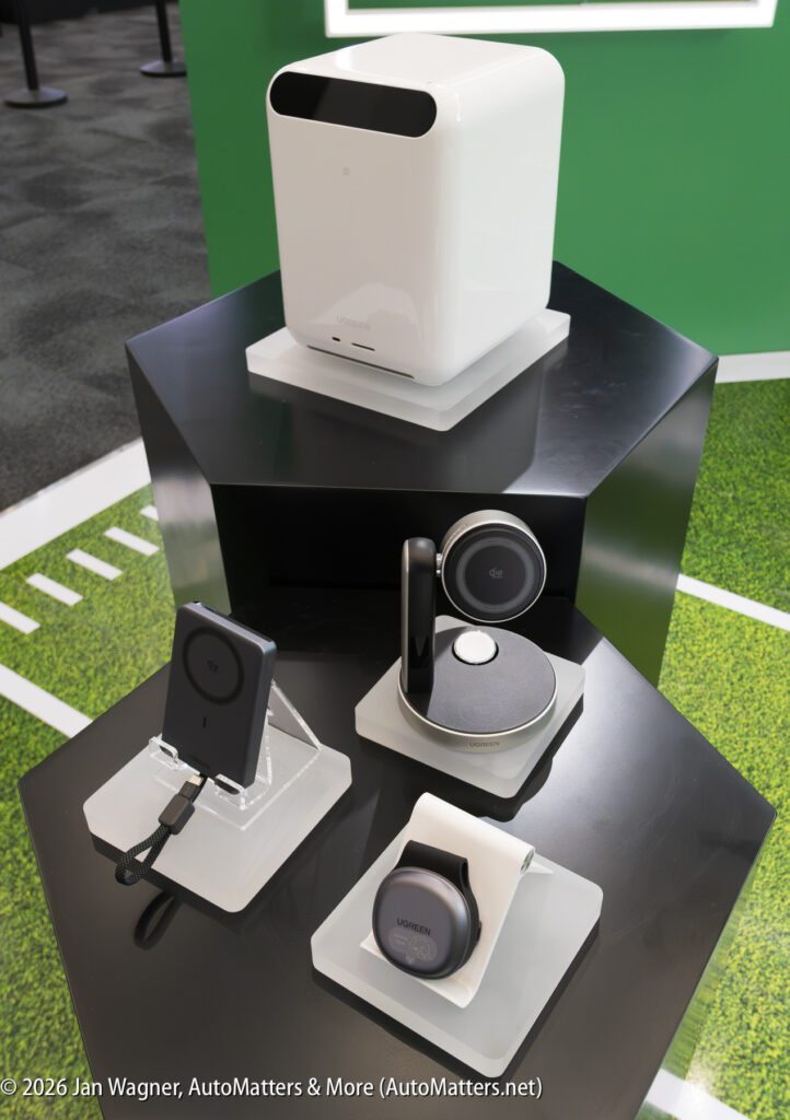 Four modern electronic devices, including chargers and smart accessories, are displayed on a black hexagonal stand with a green and white background.