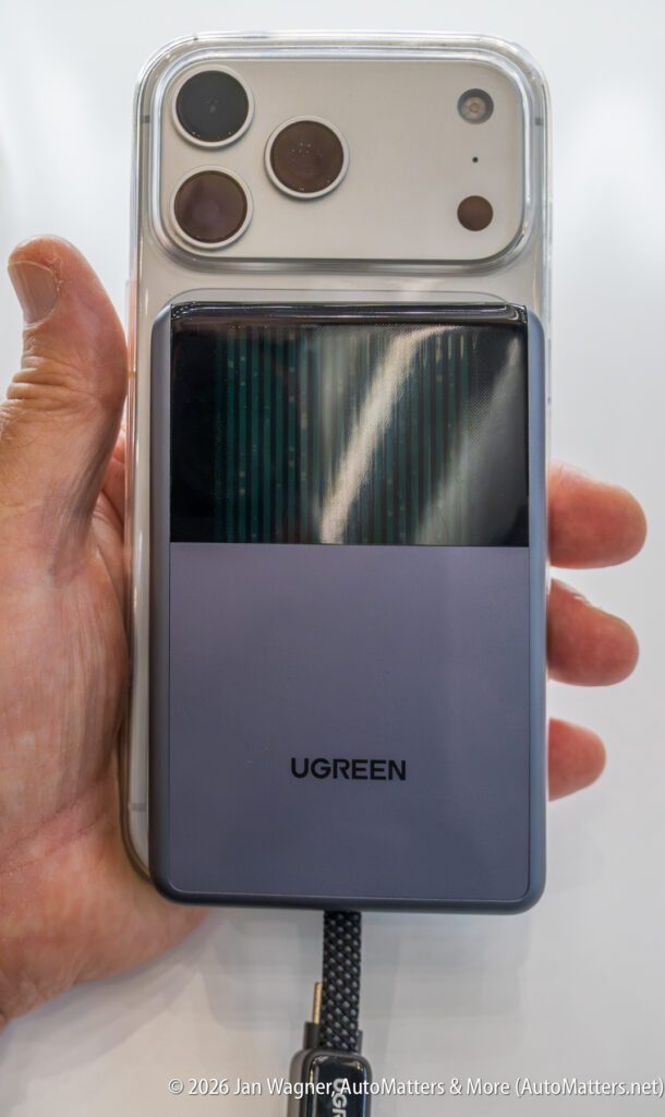 A hand holds a smartphone with a large camera module, attached to a UGREEN portable power bank via a charging cable.