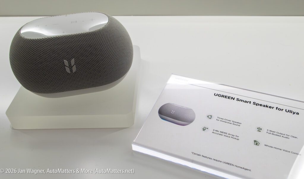 A UGREEN smart speaker is displayed on a stand next to an information card detailing its features, including dual-channel speakers, Bluetooth, and Hi-Fi audio.