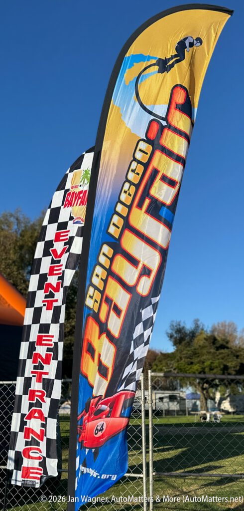 Two tall advertising feather flags for the San Diego Bayfair event, one marked “Event Entrance” and the other featuring a hydroplane boat.