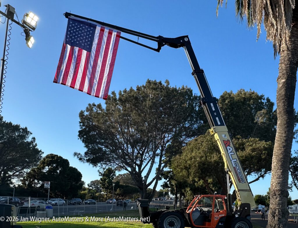 A large American flag hanging from the extended boom of a telehandler.