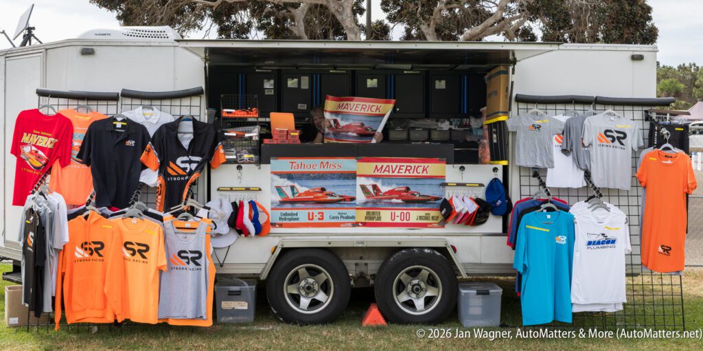 A mobile merchandise stand for Strong Racing displaying shirts, hats, and two posters featuring Tahoe Miss and Maverick hydroplane race boats.