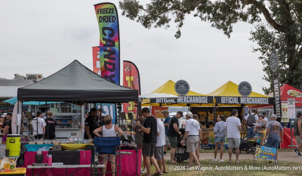 Outdoor vendor booths at an event, including a freeze-dried candy stand and an official merchandise tent.