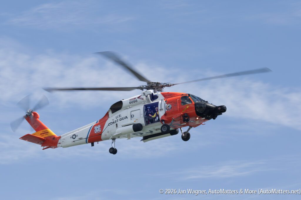U.S. Coast Guard rescue helicopter in flight against a cloudy blue sky.